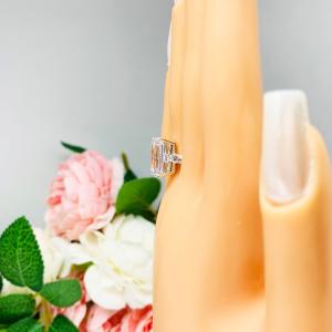 Mannequin hand with long white shimmery nails, displayed against a soft white-gray background with pink and white floral accents. The hand is wearing a sterling silver engagement ring featuring a stunning 14x10mm emerald cut cubic zirconia center stone flanked by two sparkling round CZ accents on each side.
