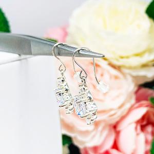 A side view of a pair of silver dangle drop art deco style earrings set with round cubic zirconia. There is one large round cz in the center, with four smaller czs mounted at the top, bottom and sides. The earrings have a scalloped edge.  The cz dangles are hanging from ear wires.