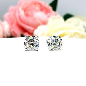 A pair of silver stud earrings with brilliant cushion cut clear cubic zirconia stones. The basket style soft claw prong earrings and are set against a white background facing forward to showcase the brilliant faceting of the czs.