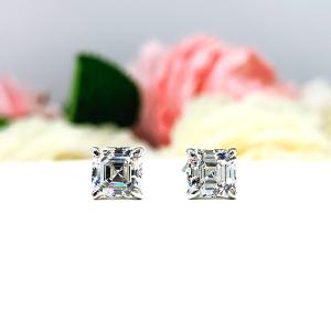 A pair of silver stud earrings with asscher cut clear cubic zirconia stones. The basket style soft claw prong earrings are on a white surface. Both earrings are facing forward showcasing the crisp, clean and tight line facets of the czs.