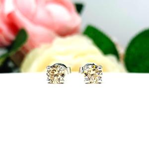 A pair of silver stud earrings set with round brilliant cut light champagne cubic zirconias.  The four prong basket earrings are on a white surface with both earrings facing front to showcase the brilliant cutting of the czs.