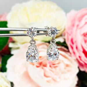 A pair of silver dangle earrings with pear-shaped clear cubic zirconia stones. The top 6-prong stud earrings have a smaller round cubic zirconia stone at the top of the drop.