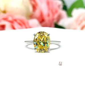 A sterling silver claw prong solitaire cathedral engagement ring featuring a well-faceted, canary yellow 10x8mm cz. Shown on a white surface with a pastel floral background.