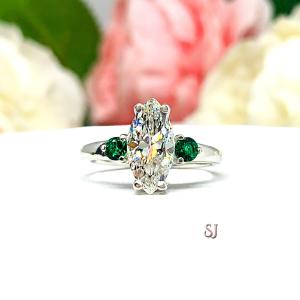 Stunning marquise-cut near colorless CZ engagement ring in sterling silver, accented with two round lab-created emeralds. Shown in size 7, the ring is nestled against a soft floral backdrop, radiating elegance and brilliance.