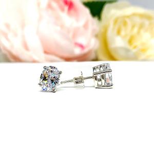 A pair of silver basket stud earrings set with oval brilliant cut cubic zirconias.  The four prong earrings are on a white surface with the left earring facing forward to showcase the clear clarity and excellent faceting of the czs and the right earring facing to the right to display the basket setting, center post and butterfly friction clasp.