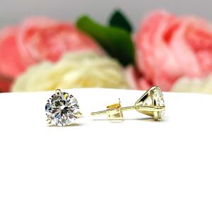 A pair of yellow gold 3-prong martini round 'near colorless' or 'G color' cubic zirconia stud earrings. The earrings are shown on a white background with the left earring facing forward showcasing the crisp faceting and clear clarity of the czs, and the right earring facing to the right displaying the center post and butterfly friction clasp.
