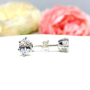 A pair of silver stud earrings set with oval brilliant cut cubic zirconias.  The 6 prong earrings are on a white surface with the left earring facing forward to showcase the brilliant cutting of the czs and the right earring facing to the right to display the center post and butterfly friction clasp.