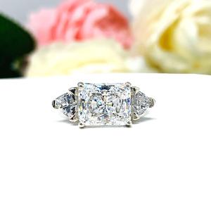 A dazzling 10x8mm radiant-cut cubic zirconia takes center stage in this horizontal engagement ring, flanked by two shimmering trillion-cut side stones. Set in luminous sterling silver, the design blends modern elegance with timeless sparkle. Its clean lines and bold brilliance make it a striking symbol of love—perfect for proposals, anniversaries, or celebrating your forever moment.