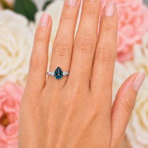 Sterling silver ring, featuring a 10x7mm London blue topaz flanked by two round moissanites, shown worn on the hand of a woman. Model image for size and styling reference — not a photo of the actual ring.