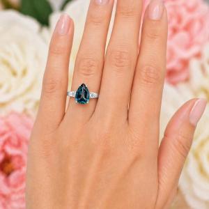 Sterling silver ring, featuring a 12x8mm London blue topaz flanked by two round moissanites, shown worn on the hand of a woman. Model image for size and styling reference — not a photo of the actual ring.