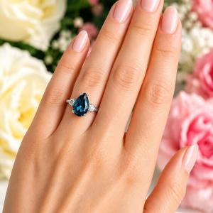 Sterling silver ring, featuring a 12x8mm pear-cut London blue topaz flanked by two round moissanites, shown worn on the hand of a woman. Model image for size and styling reference — not a photo of the actual ring