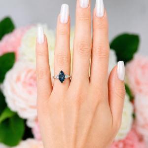 Sterling silver ring, featuring a 12x6mm marquise-cut London blue topaz flanked by two round moissanites, shown worn on the hand of a woman. Model image for size and styling reference — not a photo of the actual ring.