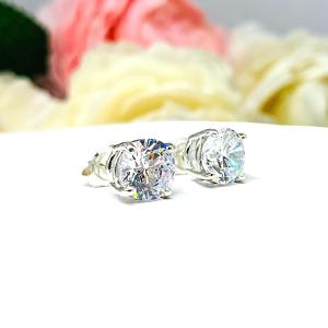 A pair of silver stud earrings set with round brilliant cut cubic zirconias.  The four prong basket earrings are on a white surface with both earrings facing slightly to the right to showcase the brilliant cutting of the czs, center post and butterfly friction clasps.