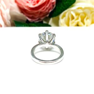 Close-up view of a 10mm near colorless (G/H color) round brilliant cut cubic zirconia solitaire engagement ring in a classic 6-prong setting. The setting is simple yet elegant, allowing the center stone to take center stage. The ring is displayed against a soft, blurred background of pastel-colored flowers, creating a romantic and delicate ambiance.