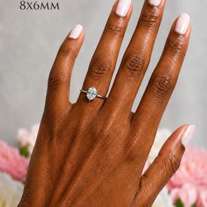 A woman's hand wearing a sterling silver 6-prong solitaire engagement ring set with an 8x6mm brilliant oval cubic zirconia. The ring features a tulip design and cathedral shank. Model image for size and styling reference — not a photo of the actual ring.
