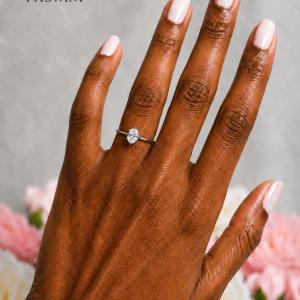 A woman's hand wearing a sterling silver 6-prong solitaire engagement ring set with a 7x5mm brilliant oval cubic zirconia. The ring features a tulip design and cathedral shank. Model image for size and styling reference — not a photo of the actual ring.