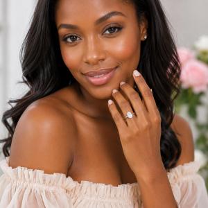 A woman wearing a sterling silver 6-prong solitaire engagement ring set with a brilliant oval cubic zirconia. The ring features a tulip design and cathedral shank. Model image for size and styling reference — not a photo of the actual ring.