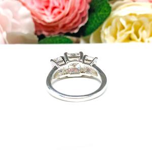 Sterling silver 3-stone engagement ring featuring a 9x7mm radiant cut cubic zirconia center stone with two 7x5mm radiant CZ side stones. The highly polished wide band tapers for comfort. Displayed on a white surface with soft floral background.