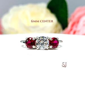 A sterling silver 3-stone ring with a round brilliant cut cubic zirconia center that radiates icy sparkle, flanked by two deep red lab-created rubies.  The text '6MM Center' is visible in the image.