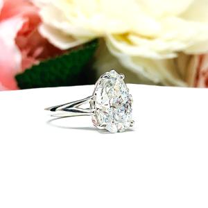 An elegant sterling silver engagement ring featuring a 13x9mm near colorless precision-cut pear cubic zirconia. Displayed on a white surface with a floral background.