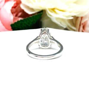 An elegant sterling silver engagement ring featuring a 13x9mm near colorless precision-cut pear cubic zirconia. Displayed on a white surface with a floral background.