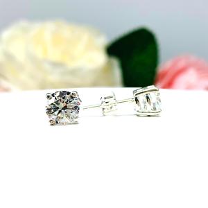 A pair of silver stud earrings set with round brilliant cut 'near colorless or 'G color' cubic zirconias.  The four prong basket earrings are on a white surface with the left earring facing forward and the right earring facing to the right to showcase the brilliant cutting of the czs, center post and butterfly friction clasp.