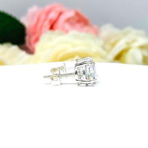 A pair of silver stud earrings set with round brilliant cut cubic zirconias.  The four prong basket earrings are on a white surface with both earrings facing to the right to showcase center post and butterfly friction clasps.