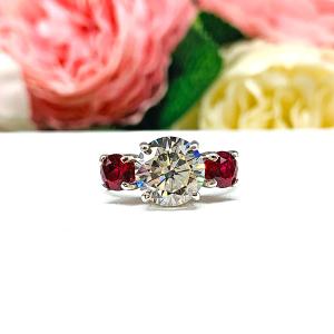 A sterling silver 3-stone ring with a 9mm near colorless round brilliant cut cubic zirconia center that radiates icy sparkle, flanked by two 5mm round deep red lab-created rubies.
