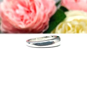 Sterling silver band featuring a 5×3 mm emerald‑cut green tourmaline set flush in a polished band, displayed on a white surface with soft pink and cream flowers blurred in the background.