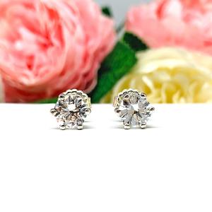 A pair of sterling silver six prong stud earrings set with round brilliant lab white sapphires. The earrings have center posts and butterfly clasps and are displayed on a white surface with a floral background.