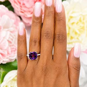 Sterling silver solitaire ring featuring a 10mm checkerboard cushion-cut vibrant African amethyst worn on a woman's hand. Model image for size and styling reference — not a photo of the actual ring