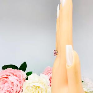 Mannequin hand with long white shimmery nails, displayed against a soft white-gray background with pink and white floral accents. The hand is wearing a sterling silver ring with an 8x6mm oval lab created padparadscha sapphire set in a 6-prong setting.