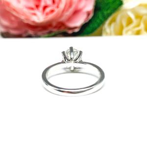 Sterling silver round-cut DEF moissanite 6-prong engagement ring. Displayed on a white surface with pink and white flowers in the background.