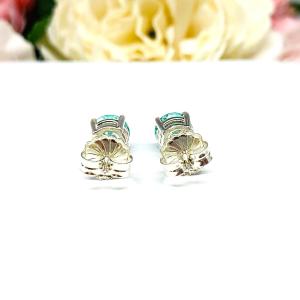 A pair of silver basket earrings set with 7mm round sea foam green lab spinels, displayed with both earrings facing to towards the back to showcase the centrally located posts and butterfly friction clasps. The earrings are shown on a white background.