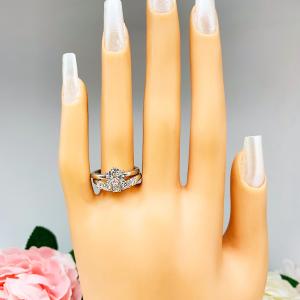 Mannequin hand with long white shimmery nails, displayed against a soft white-gray background with pink and white floral accents. The hand is wearing a sterling silver 5-stone curved wedding band featuring 3mm round precision faceted moissanite stones in prong settings. The ring is paired with a solitaire round cz engagement ring. This ring is not included.