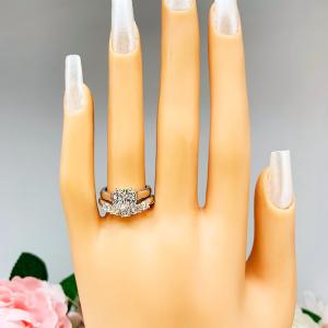 Mannequin hand with long white shimmery nails, displayed against a soft white-gray background with pink and white floral accents. The hand is wearing a sterling silver 5-stone curved wedding band featuring 3mm round precision faceted moissanite stones in prong settings. The ring is paired with a solitaire cushion cz engagement ring. This ring is not included.