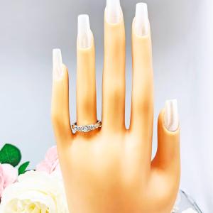 Mannequin hand with long white shimmery nails, displayed against a soft white-gray background with pink and white floral accents. The hand is wearing  a sterling silver graduated moissanite engagement ring featuring a 4mm center stone flanked by 3mm and 2.5mm side stones.