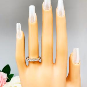 Mannequin hand with long white shimmery nails, displayed against a soft white-gray background with pink and white floral accents. The hand is wearing a sterling silver stackable 5-stone wedding band featuring 3mm round authentic moissanite stones in prong settings.