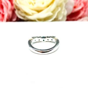 Sterling silver five-stone curved wedding band with three 3mm round lab-created emeralds and two 3mm round DEF moissanites, shown against a soft floral background.
