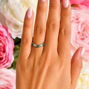 A woman's hand wearing a sterling silver five-stone curved wedding band with three 3mm round lab-created emeralds and two 3mm round DEF moissanites.