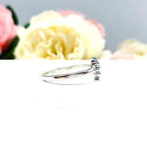 Sterling silver cluster ring featuring four 3mm round light blue aquamarine gemstones. Displayed against a soft-focus floral background, the ring sparkles with contrast and elegance.