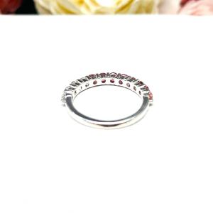 Sterling silver twelve stone band set with 2.5mm round gemstones in this configuration: four white topaz, four pink tourmaline and four light pink tourmaline set in a shared prong setting, displayed on a white surface with soft-focus pastel flowers in the background.
