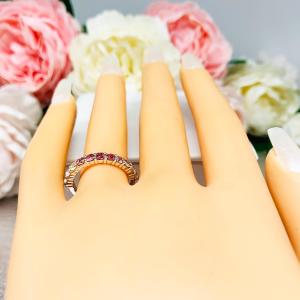 Mannequin hand with long white shimmery nails, displayed against a soft white-gray background with pink and white floral accents. The hand is wearing a sterling silver  twelve stone band set with 2.5mm round gemstones in this configuration: four white topaz, four pink tourmaline and four light pink tourmaline set in a shared prong setting.