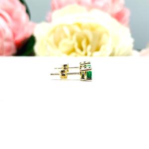 A pair of 14k yellow gold stud earrings set with 4mm round natural emerald gemstones. The four prong basket earrings are on a white surface with both earrings facing to the right to showcase the center post and butterfly friction clasps.