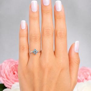 A woman's hand wearing a sterling silver cluster ring featuring four 3mm round light blue aquamarine gemstones. Displayed against a soft-focus floral background, the ring sparkles with contrast and elegance. Model image for size and styling reference — not a photo of the actual ring.