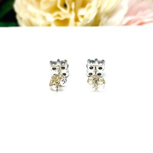 Sterling silver cluster earrings featuring four 3mm round light blue aquamarine gemstones. Displayed against a soft-focus floral background, the earrings sparkle with contrast and elegance.