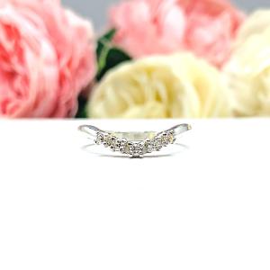 Sterling silver 5-stone curved wedding band featuring 2mm round precision faceted moissanite stones in prong settings, displayed against a soft floral background.