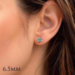 Woman wearing 6.5mm round blue moissanite martini stud earrings. Model image for size and styling reference — not a photo of the actual earrings.