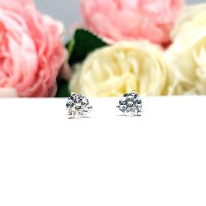 A pair of sterling silver 3-prong martini stud earrings with 6mm colorless old European cut cubic zirconias. The earrings are resting on a white surface with a background of pink and white flowers.