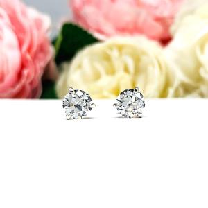 A pair of sterling silver 3-prong martini stud earrings with 6.5mm colorless old European cut cubic zirconias. The earrings are resting on a white surface with a background of pink and white flowers.